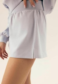 Jasnofioletowa mini spódnica z prążkowanego materiału, z marszczonym pasem i bocznymi rozcięciami. Posiada małe logo na końcu. Miękka tekstura i swobodny design.