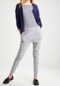 Cardigan azul marino, top a rayas y pantalones gris claro ajustados con bolsillos. Mocasines negros completan el conjunto. Texturas suaves, diseño casual.