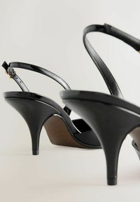 Fekete, magas sarkú szandálok fényes felülettel, vékony, állítható pántokkal és formázott talppal. Elegáns, ívelt sarokdizájn jellemzi.
