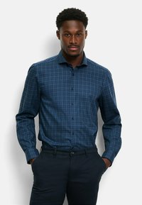 Blau karierte Hemdbluse mit langen Ärmeln und Button-Down-Kragen. Sie zeichnet sich durch eine Mischung aus dunkelblauen und hellblauen Quadraten aus und besteht aus glattem Stoff.