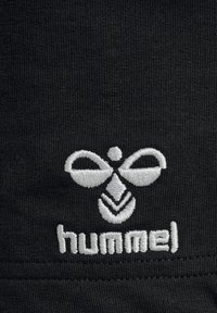 Tessuto nero con finitura strutturata che presenta un logo ricamato bianco. Il logo è composto da forme simmetriche e dalla parola "hummel".