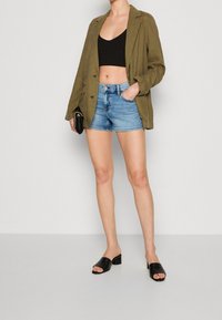 Olivgrön oversize blazer, svart crop top, ljusblå denimshorts och svarta klackskor med blockklack. Släta texturer och enkel design.