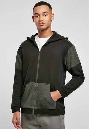 Haut à zip noir avec des accents gris sur les manches et la poche. Comprend une poche kangourou, une capuche et des poignets côtelés. Fabriqué à partir d'un tissu doux.
