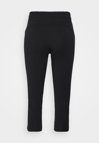 Svarta midjereglerade caprig leggings sedd bakifrån med en slät, figurnära design och ankellånga avslut på en vit bakgrund.