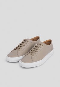 Zapatillas de cuero beige con cordones planos, una superficie lisa, suela de goma blanca y un diseño minimalista. Los acentos incluyen un interior en color marrón.