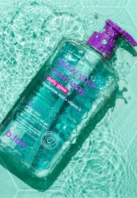 Clear teal pump bottle labeled "daily glow" hyaluronic acid + vitamin C gel, floating in water with light reflections and droplets.