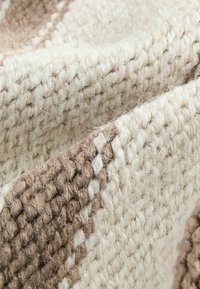 Gros plan sur un tissu en tricot texturé avec des rayures beige et marron clair, montrant des fibres de laine douces et duveteuses ainsi que les détails du motif tissé.