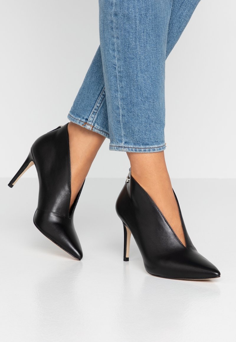 Chaussures à talons hauts en cuir noir avec un bout pointu et un design en V profond. Elles sont dotées d'une fermeture éclair à l'arrière et d'un talon stiletto fin.