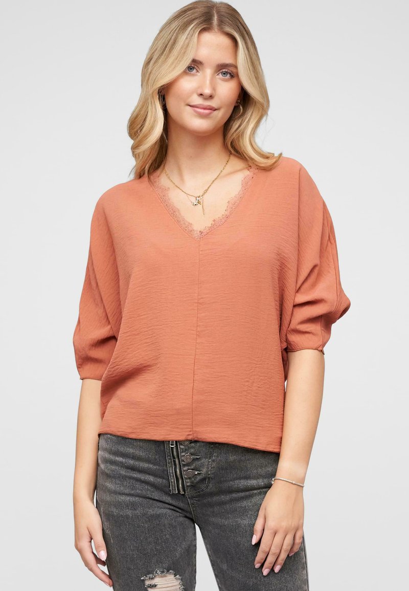 Korte mouwen, v-hals top in terracotta met een kantafwerking, geweven stof. Gemaakt met donkere, versleten jeans met een ritsdetail.