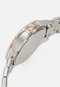 Reloj de acero inoxidable plateado con una caja redondeada y un bisel de oro rosa. Cuenta con una corona texturizada y una pulsera de metal conectada.