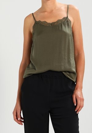 Satynowy top na cienkich regulowanych ramiączkach w kolorze oliwkowej zieleni z koronkową lamówką, o luźnym kroju. W zestawie z czarnymi spodniami z elastycznym pasem.