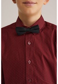 Rood patroonstrik met kleine witte vierkanten, dichtgeknoopt met roze knopen, gecombineerd met een zwarte strik aan de kraag.