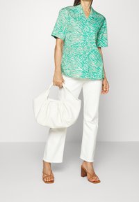 Blouse verte à manches courtes avec des rayures blanches en forme de zèbre, associée à un pantalon blanc à jambes droites et un sac en tissu crème. Sandales à talons carrés marron.