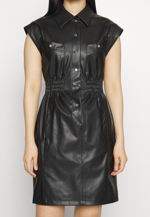 Hihaton musta keinonahkainen napillinen mekko, jossa on terävä kaulus, kaksi rintataskua, joustava vyötärödetaili ja polvipituinen helma.