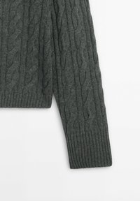 Manche de pull tricoté gris foncé avec un motif torsadé et un poignet côtelé, présenté sur un fond blanc.