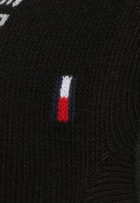 Čierna pletená tkanina s horizontálnym bielym textom a malým vyšitým logom s červenými, bielymi a modrými vertikálnymi pruhmi.