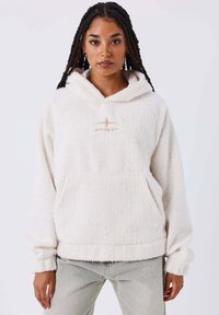 Sudadera de felpa blanca con textura acanalada, bolsillo canguro y logo bordado. Presenta un corte holgado y puños amplios.