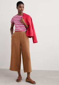 Chemise à rayures à manches courtes en rouge et bleu clair, assortie à un pantalon large taille haute marron et des sandales strappy marron. Veste rouge drapée sur le bras.
