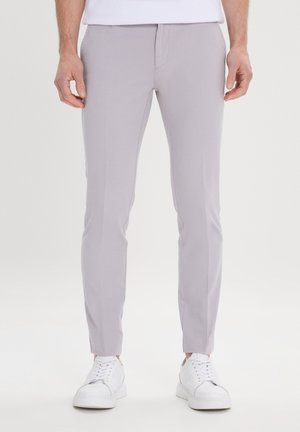Pantalons slim gris clair en tissu texturé, dotés de poches avant et d'une taille lisse, associés à des baskets blanches.