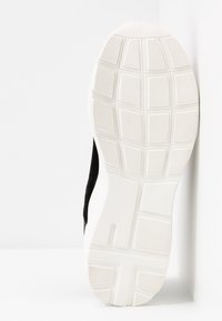Semelle d'une chaussure de sport noire et blanche avec un motif de bande de roulement géométrique texturé pour une meilleure adhérence, présentée sur un fond blanc.