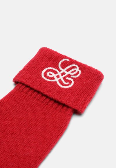 Calcetines rojos de lana con textura acanalada, con un logo bordado en blanco en el puño doblado. El tejido parece suave y grueso.