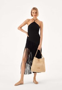 Fekete bordázott nyakbakötős ruha bojt részlettel, szalmakézitáskával és barna lapos szandállal párosítva, hasítékkal a légies megjelenésért.