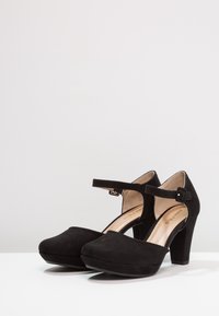 Czarne zamszowe buty na wysokim obcasie z zaokrąglonym noskiem, paskiem na kostce i detalem z klamrą, z platformą i teksturowanym wykończeniem.