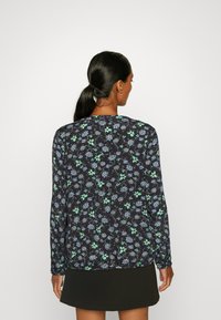 Blusa de manga longa com um padrão floral escuro com realces azuis e verdes, apresentando um decote redondo e punhos franzidos. Textura de tecido suave.