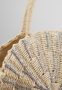 Sac à main rond en paille tissée avec des accents de fil argenté et une poignée courte et solide sur un fond neutre.