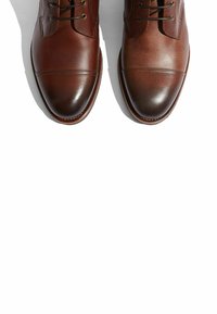Zapatos de cuero marrón con un acabado suave, punta redondeada y diseño de cordones. Presentan costuras contrastantes a lo largo de la parte superior y un tacón texturizado.