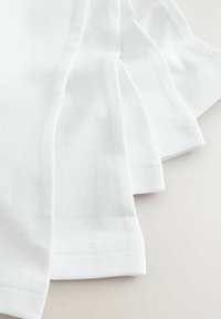 Vier opgevouwen witte katoenen T-shirts met korte mouwen, met een gladde textuur en keurig gestikte zomen.