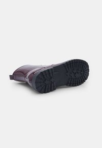Stivaletto in gomma bordeaux con finitura lucida, dotato di una suola nera testurizzata con scanalature profonde per un buon grip e un tassello posteriore per indossarlo facilmente.