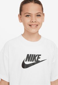 Balta trumpa rankovėmis marškinėliai, pagaminti iš medvilnės, su dideliu juodu Nike logotipu priekyje, laisvo silueto ir minkštos tekstūros.