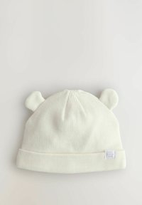 Biała dzianinowa czapka beanie o prążkowanej strukturze, z dwoma zaokrąglonymi akcentami przypominającymi uszy na górze oraz z zagiętym daszkiem z małą metką.