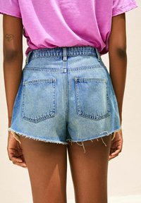 Lichte blauwe denim shorts met een rafelige zoom, hoge taille en twee achterzakken worden gedragen met een roze T-shirt.