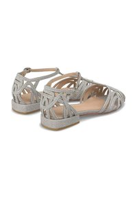 Srebrne płaskie sandały na paski z plecionym wzorem i błyszczącymi akcentami oraz niskim obcasem. Otwarty tył i wyściełane wnętrze.
