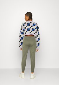 Cropped, multicolored checkerboard sweater with purple, black, and blue pattern; paired with green leggings and white sneakers.