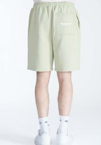 Pantaloni corti verde chiaro realizzati in tessuto morbido, con cintura elastica, tasche laterali e una tasca posteriore con patch con il logo "MULTIPLY".