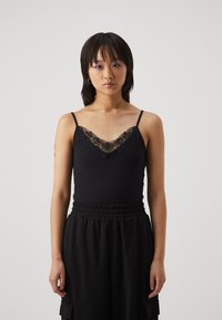 Black tank top with lace trim along the neckline, featuring thin straps and a fitted design, paired with loose black pants.