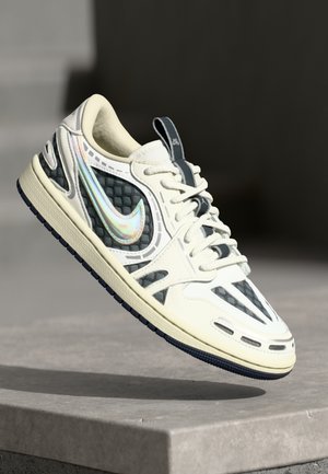 White and black Nike sneaker with iridescent swoosh, laces, and patterned panels, suspended above a concrete surface.