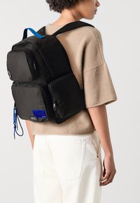 Black nylon backpack with multiple zippered pockets, blue accents, comfortable padded straps, and a distinct circular logo on the upper pocket.