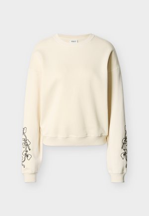 Kremfarget genser med lange ermer og ribbestrikkede mansjetter og kant, med svarte blomstrete linjetegninger på begge ermer.