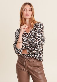 Leopardenmuster-Pullover aus weichem Material, V-Ausschnitt, lange Ärmel, kombiniert mit braunen Leder-Jogginghosen mit Taschendetails.