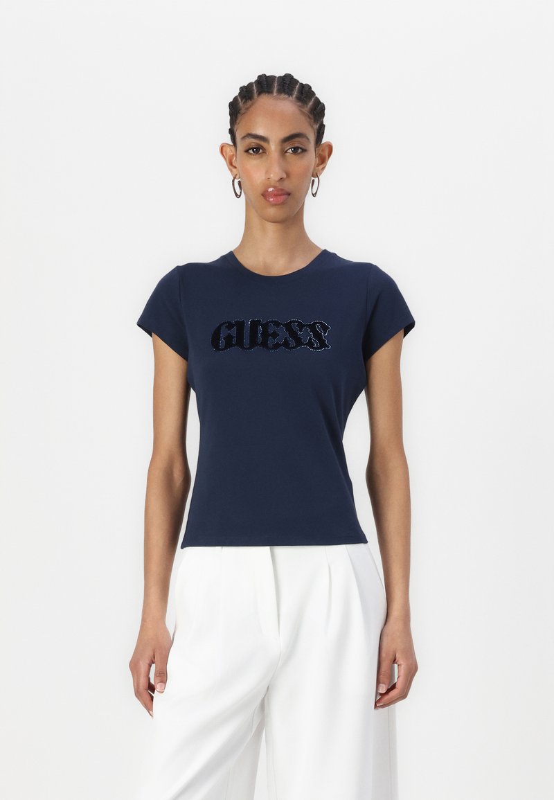 Tamsiai mėlynas prigludęs marškinėliai, pagaminti iš minkštos medvilnės, su blizgiu „GUESS“ logotipu tekstūruotame dizaino. Trumpomis rankovėmis ir apvali iškirpte.