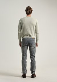 Suéter de manga larga verde claro con cuello redondo, combinado con jeans de mezclilla azules. Modelo de espaldas, mostrando la textura de punto y los detalles de los bolsillos traseros.