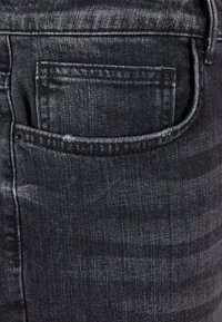 Černé džíny z denimu s zadní kapsou, s mírně vybledlou texturou a zesíleným švem kolem okrajů.