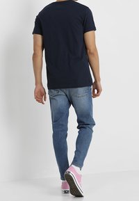Camiseta de manga corta azul marino combinada con vaqueros azul claro y zapatillas rosas. La tela parece suave, con un diseño sencillo y sin logotipos visibles.