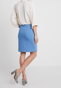 Jupe crayon bleu clair à la coupe ajustée, texture lisse et détails de coutures subtiles. Associée à des chaussures à talons imprimé peau de serpent.