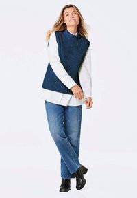 Navyfarbener, strukturierten Strick-Sleinenshirt über einem weißen Shirt, kombiniert mit blauen Jeans und schwarzen Stiefeletten. Einfaches Design mit lässiger Passform.