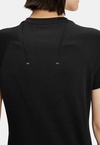 Camisa negra de manga corta con un cuello alto y cordón ajustable en la parte trasera. Textura suave con detalles de diseño mínimos.